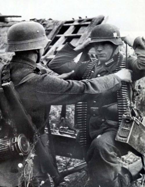 A soldier is seen on the right using a Tragegurt 34 with 2 Patronenkasten. The soldier on the left is carrying the Lauschützer 34. Both are part of an MG crew.